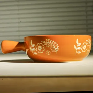 Primo piano della ciotola da forno in ceramica arancione con motivo floreale bianco.
