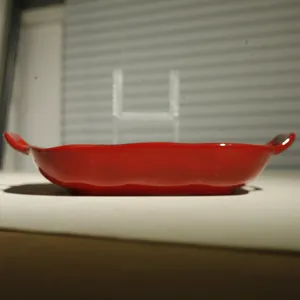Red ceramic baking dish detail, dual handle oven tray for kitchen cooking and food serving.