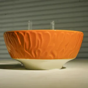 Orangefarbene Keramikschale Detail mit strukturierter Aussenwand und weissem Boden für Tisch.