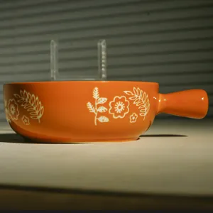 Ciotola da forno in ceramica arancione con motivo floreale bianco e manico, dettaglio.