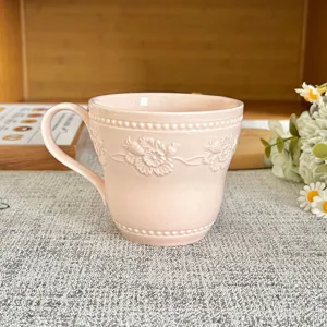 Tazza da caffè in ceramica rosa goffrata con rilievo floreale e manico per uso quotidiano.