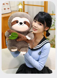 Simpatico peluche bradipo con ramo e foglie, tenuto da una modella in ambiente interno.
