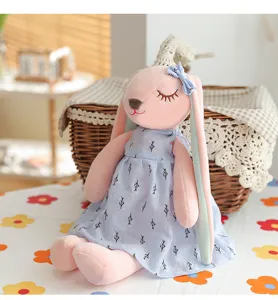 Detail view of a soft plush lop-eared bunny toy wearing a blue dress and bow, sitting cozy.