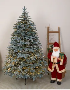 Scena con albero di Natale Noble Fir innevato con luci calde accanto a un Babbo Natale