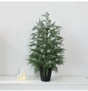 Artificial potted cedar Christmas tree on a white mantel with a lit miniature house