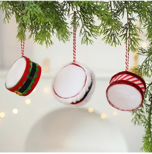Close-up of three festive mini drum ornaments hanging on lush green pine branches