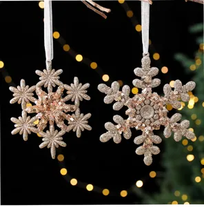 Detailopname van twee champagne goudkleurige glinsterende sneeuwvlok kerstornamenten.