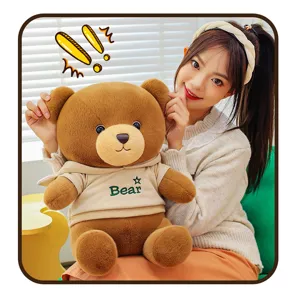 Cute brown teddy bear plush toy wearing soft beige hoodie, detail view in cozy room setting.