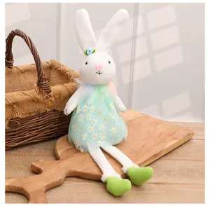 Close-up of white Easter bunny plush toy wearing a green floral dress on a wooden surface