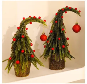 Close-up of two mini bent Christmas trees with red ornaments on a white shelf.