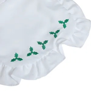 Close-up detail of white Christmas costume fabric featuring green embroidered holly leaves and ruffles.