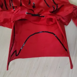 Primo piano del tessuto di raso rosso, delle finiture di paillettes nere e degli occhielli.