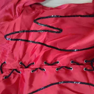 Dettaglio del tessuto del costume rosso con paillettes nere e occhielli di allacciatura.