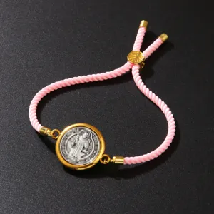 Detailed close-up view of a pink braided rope bracelet with a vintage gold coin pendant