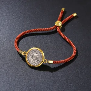 Detail of an adjustable orange braided rope bracelet with a gold vintage medal pendant