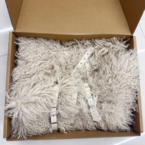 Close-up of white faux fur punk snow boots with multiple leather straps inside a cardboard box