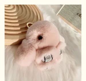 Gros plan d'un porte-clés lapin en peluche rose avec détails en strass et anneau doré.