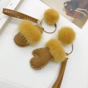 Macro view of cute fur mitten bag charms with yellow pom-poms on a white background.
