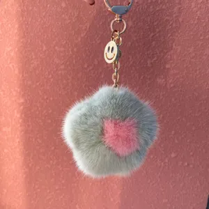 Close-up of a soft mink fur flower keychain with a gold smiley face charm and metal clasp