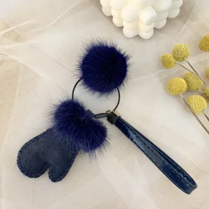 Close-up of navy blue mink fur mitten keychain with fluffy pom-poms on mesh background.
