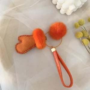 Detail view of a cute orange fur glove keychain charm with fluffy mink fur pom-poms for bags.