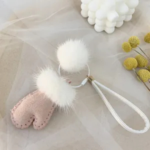 Macro detail of cute pink mitten-shaped bag charm with white fluffy mink fur pom-poms