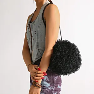 Detail view of a black fluffy faux Mongolian lamb fur cloud bag on a shoulder.