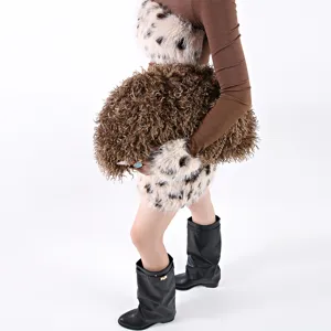 Close-up detail of a large brown curly faux fur cloud bag held by a fashion model