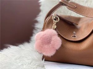 Detail of pink mink fur flower charm attached to a brown leather handbag on fur rug