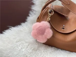 Close-up of pink mink fur flower bag charm with gold chain on brown leather bag.