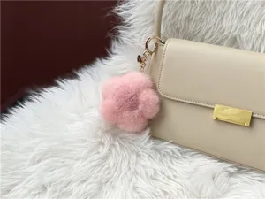Close-up of a luxury pink mink fur flower-shaped keychain accessory on a beige handbag.
