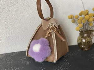 Detail of a purple and white mink fur flower keychain attached to a brown suede bag.