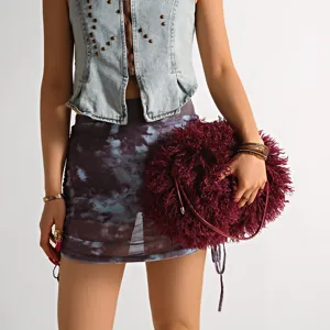 Detail view of a burgundy fluffy faux shearling cloud clutch bag held by a model