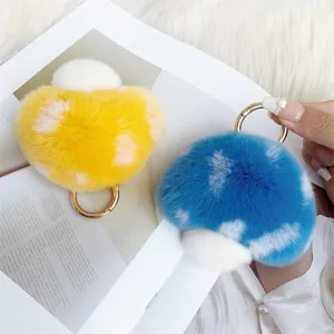 Close-up view of two soft plush mushroom charms in yellow and blue with gold rings.