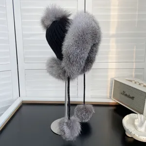 Primer plano de un gorro de punto negro con lujoso ribete y pompones de piel de zorro gris.
