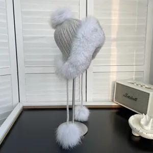 Detalle de gorro de invierno de punto gris con ribete de piel de zorro y pompones suaves