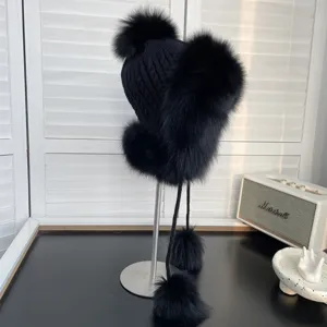 Vista detallada de un gorro de aviador de punto negro con lujosos pompones de piel de zorro