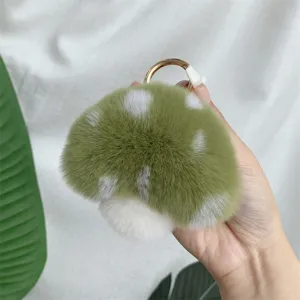 Close-up of a soft green and white plush mushroom keychain with a gold ring.