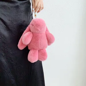 Pendentif lapin en peluche rose doux tenu à la main devant un mur blanc texturé