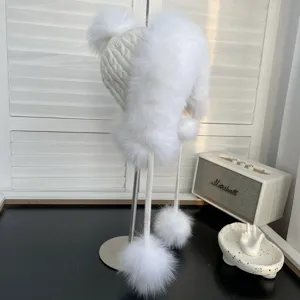 Detalle de gorro de aviador de punto blanco con pompones de piel sintética y orejeras.