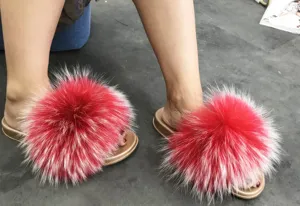 Close-up detail of stylish red raccoon fur slippers with metallic gold PVC soles worn on feet