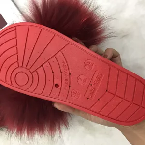 Primo piano di ciabatte in pelliccia rossa con suola in PVC antiscivolo e taglie incise.