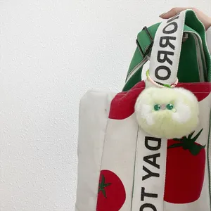 Macrodetail van een schattige groene pluche kattenhanger aan een canvas tas met tomatenprint.