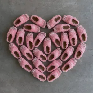 Creative heart-shaped layout of stylish pink furry slippers with silver metallic claws.