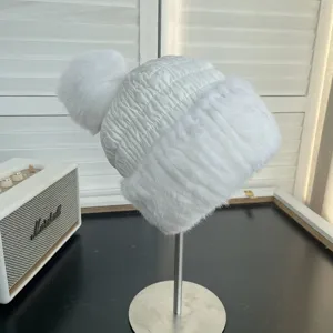 Detailed side view of a white women's winter hat with a fluffy fox fur pom-pom and mink trim
