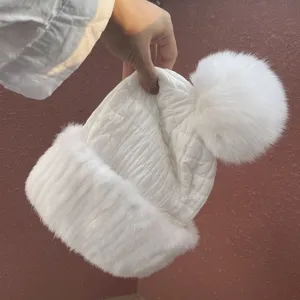 Close-up of white quilted winter hat with plush fur trim and large pom-pom detail
