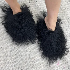 Close-up view of fluffy black Mongolian sheep fur slides worn on a textured rug.