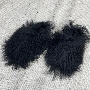 Macro detail of black Mongolian lamb fur slides featuring long curly hair texture