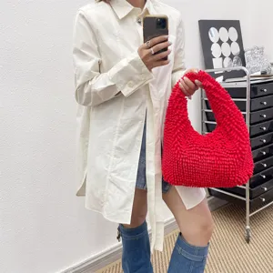 Sac à main rouge vif à texture pelucheuse porté par un mannequin dans un cadre intérieur moderne.