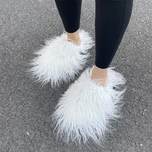Witte pluizige Mongoolse imitatiebont slippers met zwarte legging op een asfaltachtergrond.